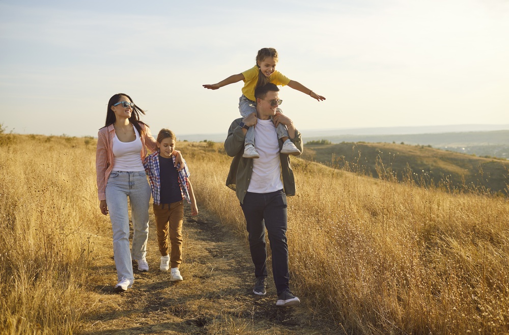 Family walking through a golden field at sunset with their child on dad’s shoulders