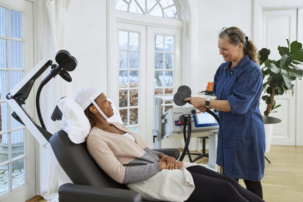 Patient seated in a TMS treatment chair speaking with a provider
